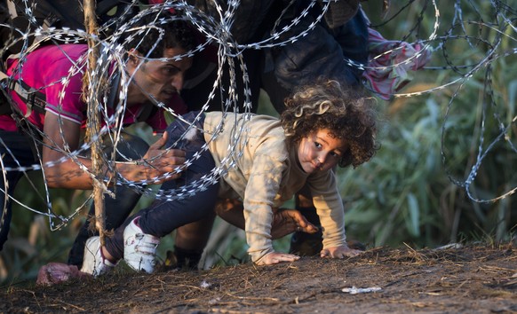 FILE - In this Thursday, Aug. 27, 2015 photo, a child is helped cross from Serbia to Hungary through the barbed wire fence near Roszke, southern Hungary. Round the clock, thousands of refugees cross d ...