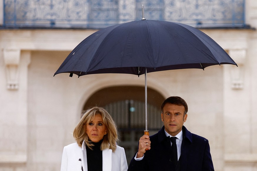 epa10948864 French President Emmanuel Macron (R) holds an umbrella as he walks with his wife Brigitte Macron during the inauguration of the Cite internationale de la langue francaise, a cultural and l ...
