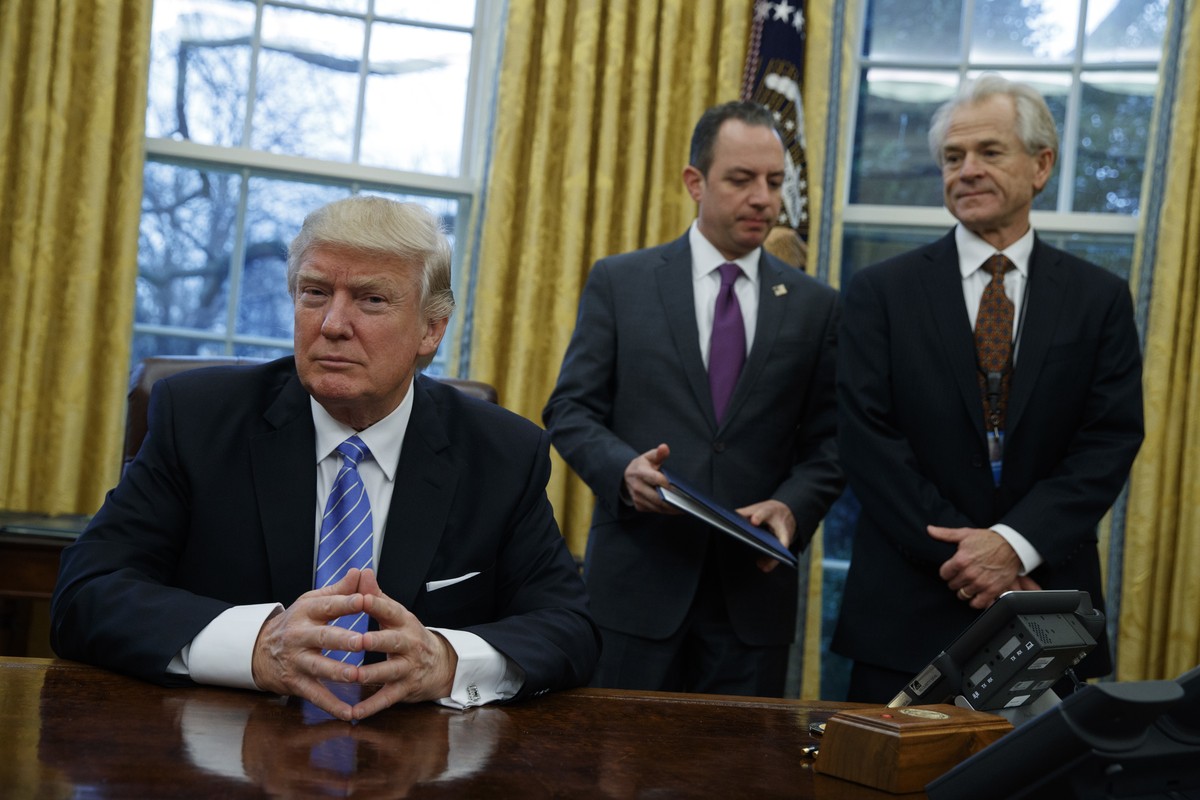 National Trade Council adviser Peter Navarro, right, and White House Chief of Staff Reince Priebus, center, await President Donald Trump's signing three executive orders, Monday, Jan. 23, 2017, i ...