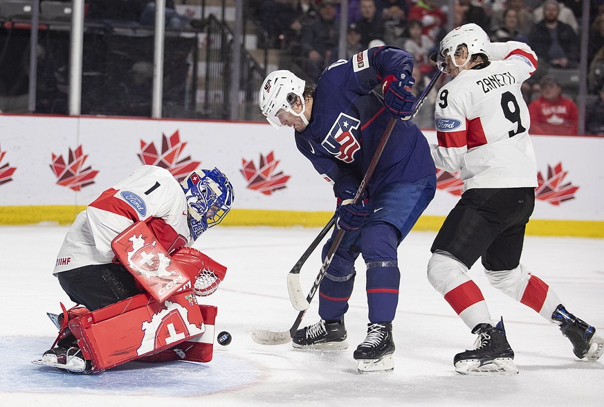 Switzerland goaltender Alessio Beglieri makes a save as United States&#039; Tyler Boucher and Switzerland&#039;s Brian Zanetti work in front of him during the second period of an IIHJ world junior hoc ...