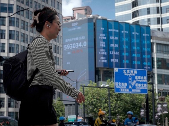 epa10799558 A woman walks on the street, in front of the large screen showing latest stock exchange data, in Shanghai, China, 14 August 2023. China&#039;s largest private developer, Country Garden, sa ...