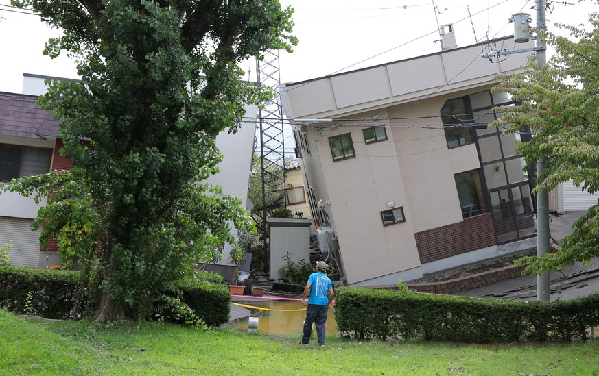 epa07002228 A man looks at an inclined house after a powerful earthquake and following liquefaction in Sapporo, Hokkaido, northern Japan, 07 September 2018. At least eight people died and almost 30 pe ...