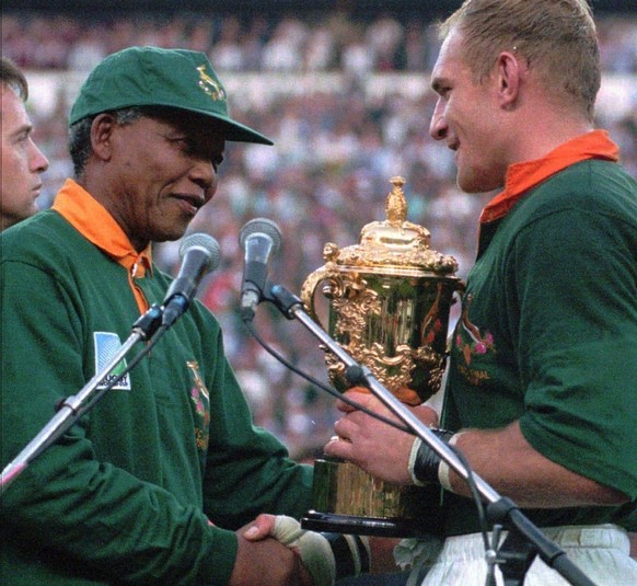 FILE - This June 24, 1995, file photo shows South African rugby captain Francios Pienaar, right, receiving the Rugby World Cup trophy from President Nelson Mandela, left, who wears a South African rug ...