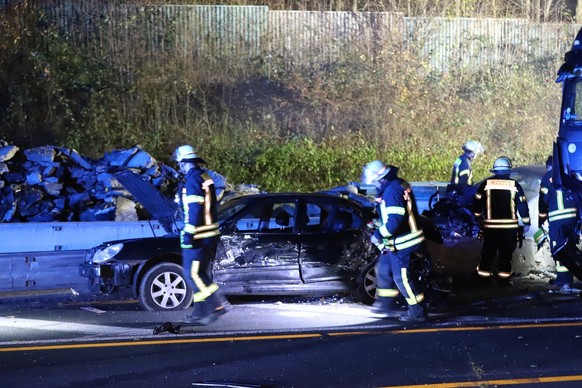 30.11.2024, Nordrhein-Westfalen, Hagen: Einsatzkr�fte der Feuerwehr stehen neben einem besch�digten Auto auf der Autobahn 1 bei Hagen an der Unfallstelle. Nach einer Chaosfahrt �ber mehrere Autobahnen ...