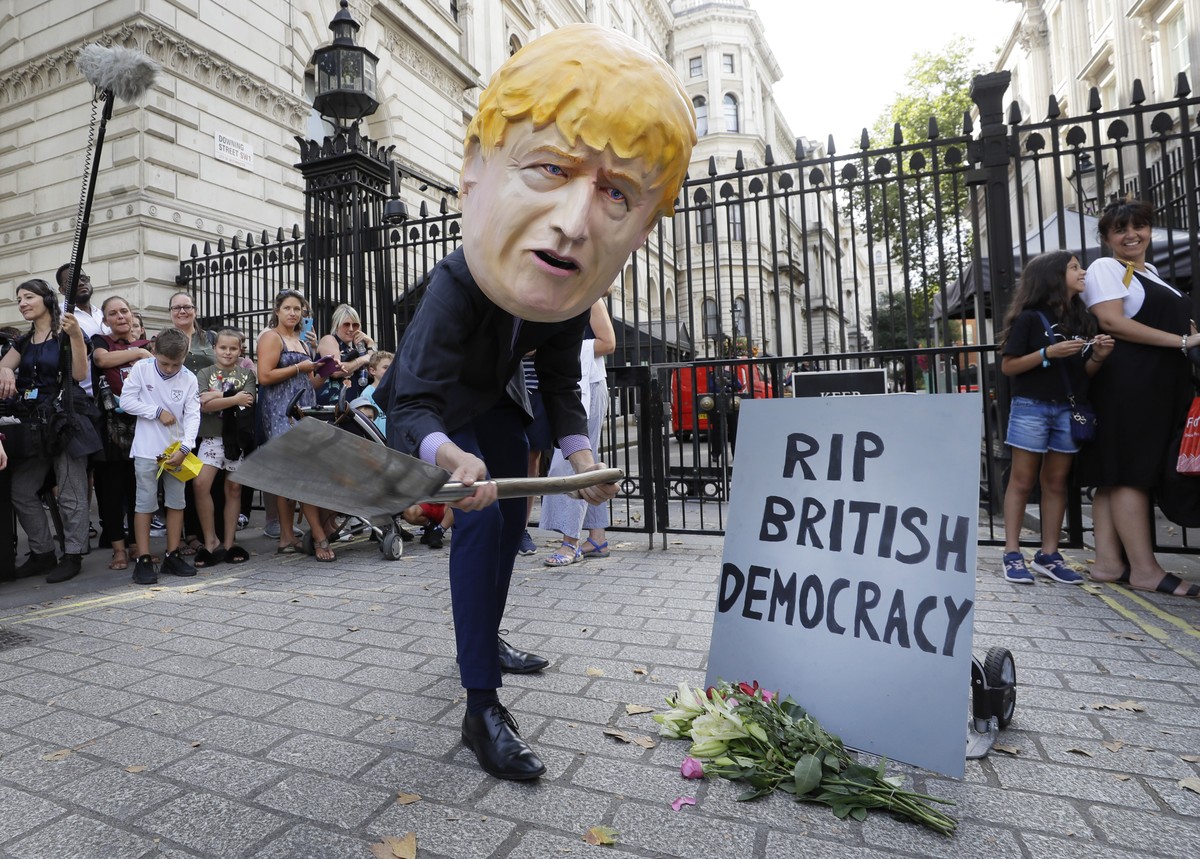 A man in a giant Boris Johnson 'head' digs a grave at the foot of a pretend tombstone outside Downing Street in London, Wednesday, Aug. 28, 2019. Britain's Queen Elizabeth II has approv ...