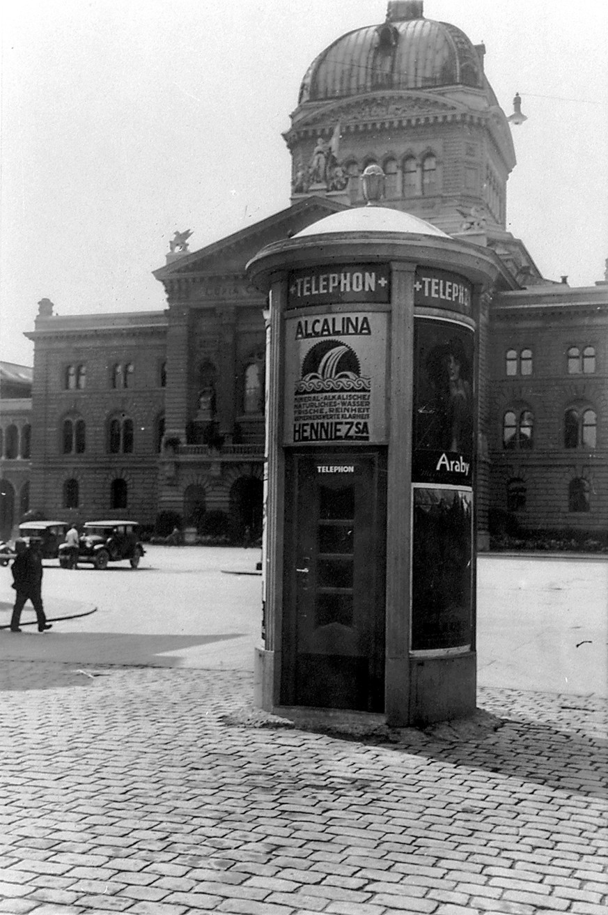 Eine öffentliche Sprechstation in einer Plakatsäule beim Bundeshaus in Bern. Der Anrufer ist gut vor neugierigen Blicken geschützt. Aufnahme von ca. 1930.