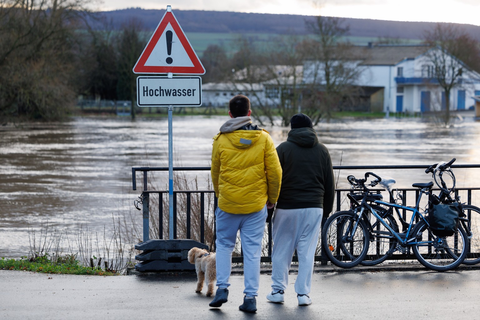 26.12.2023, Nordrhein-Westfalen, H�xter: Spazierg�nger mit Hund stehen vor einem Schild �Hochwasser�. Die Weser ist hier �ber das Ufer getreten. Der Wasserstand der Weser ist in den vergangenen Tagen  ...