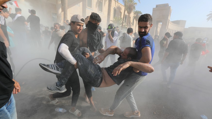 epa10145987 Supporters of Iraqi Shiite cleric Muqtada al-Sadr help injured protesters during clashes with anti-riot forces near the office of prime minister, Baghdad, Iraq, 29 August 2022. Several peo ...