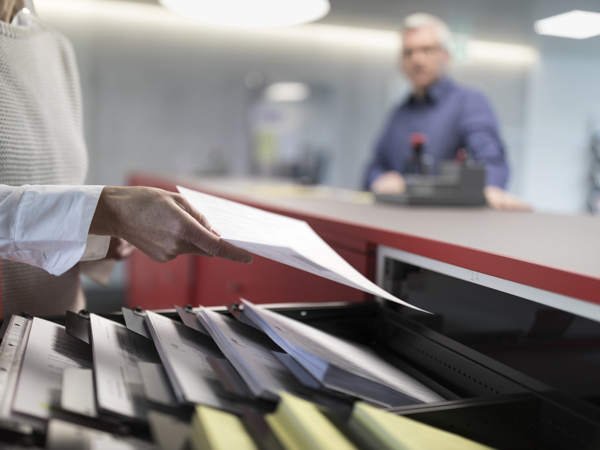 ARCHIV - ZUR WINTERSESSION 2019 MIT DEM THEMA ARBEITSLOSENVERSICHERUNG, STELLEN WIR IHNEN FOLGENDES BILDMATERIAL ZUR VERFUEGUNG - [Symbolic Image, Staged Picture] A receptionist takes a document out o ...