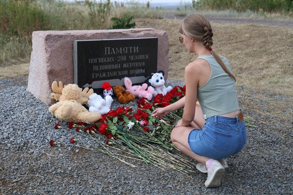 epa11483968 A woman lays flowers at the memorial to the victims during a mourning ceremony at the crash site of the MH17 plane, on the 10th anniversary of the disaster, near village of Grabovo, around ...