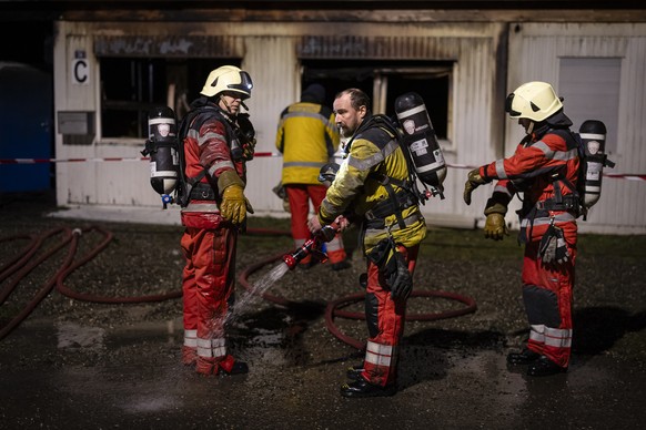 Einsatzkraefte der Feuerwehr reinigen ihre Kleidung nach einem Einsatz auf einem Brandplatz einer Unterkunft fuer Asylsuchende auf dem Areal des Alten Bahnhofs in Buchs, am Samstag, 3. Februar 2024 in ...