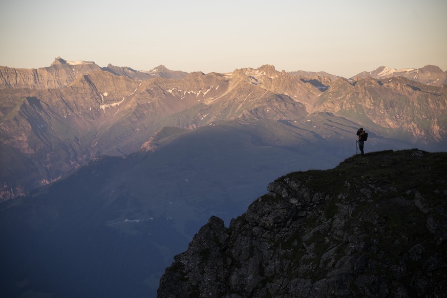 Ein Schaefer steht auf einem Felsvorsprung mit Blick auf den Ringelspitz und wartet darauf, dass 1400 Schafe von einer Weide zur anderen wandern, am Samstag, 10. August 2024, beim &quot;Schafuebergang ...