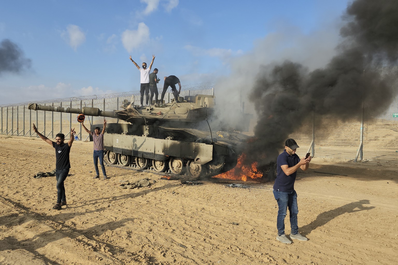 Palestinians celebrate by a destroyed Israeli tank at the Gaza Strip fence east of Khan Younis Saturday, Oct. 7, 2023. The militant Hamas rulers of the Gaza Strip carried out an unprecedented, multi-f ...