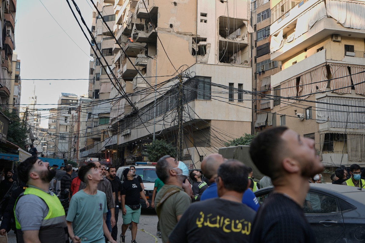 People looking up to the sky for an Israeli drone as they gather at the site where an Israeli airstrike hit at apartment, background, on Dahiyeh in the southern suburb of Beirut, Sunday Nov. 23, 2025. ...