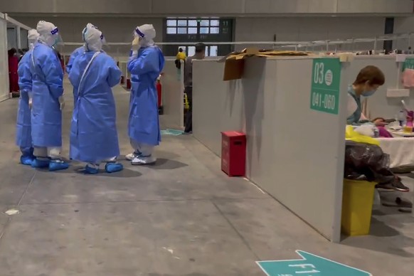 In this image taken from video provided by Beibei, who asked to be identified only by her given name, medical workers wearing protective suits chat as a resident takes a rest at the National Exhibitio ...