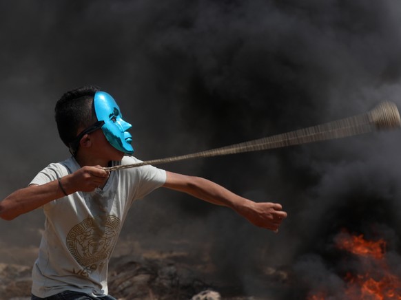 epa09380366 Palestinian protester wearing a mask uses slingshot to hurl stones during clashes after a demonstration against the expansion of the new Jewish outpost of Eviatar on the lands of Beita vil ...