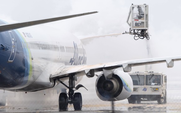 A ground crew member de-ices an Alaska Airlines passenger jet at Kansas City International Airport on Thursday, Dec. 22, 2022, in Kansas City, Mo. (Nick Wagner/The Kansas City Star via AP)