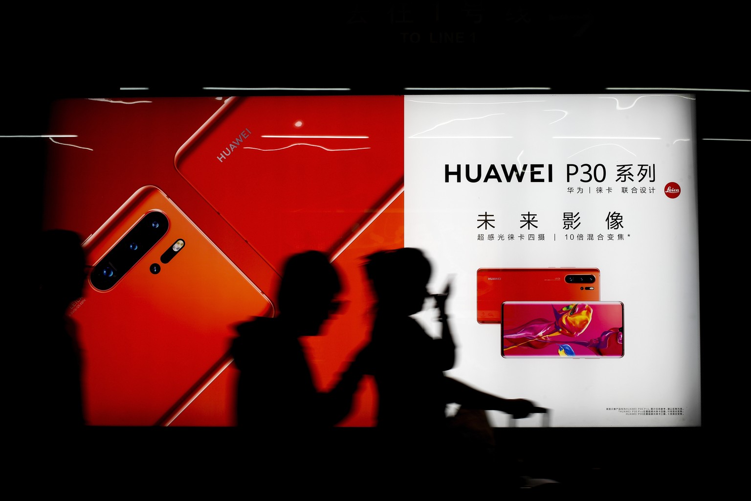 Commuters walk by the new Huawei P30 smartphone advertisement on display inside a subway station in Beijing Monday, May 13, 2019. China's intensified tariff war with the Trump administration is threat ...