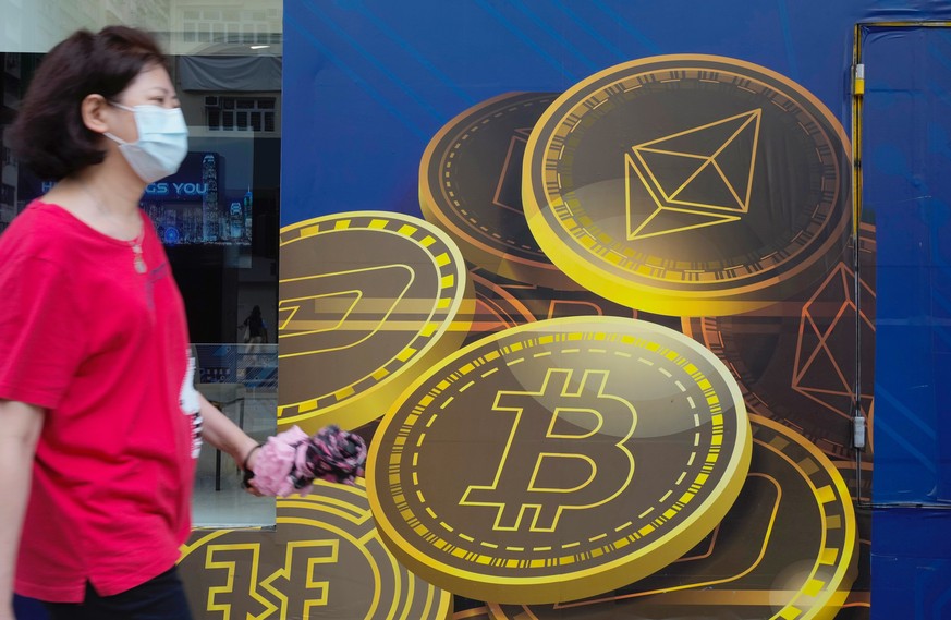 FILE - In this June 1, 2021, file photo, a woman walks past an advertisement for the Bitcoin cryptocurrency in Hong Kong. China