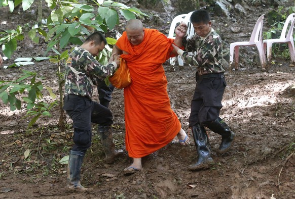 A Buddhist monk, helped by Thai rescues, walks after praying near a cave complex where 12 boys and their soccer coach went missing, in Mae Sai, Chiang Rai province, in northern Thailand, Sunday, July  ...