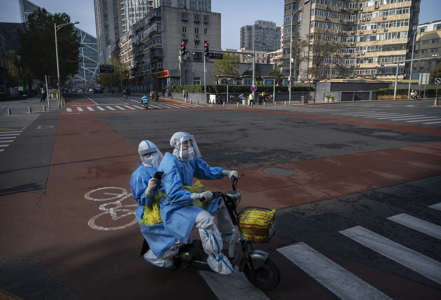 BEIJING, CHINA - NOVEMBER 23: Epidemic control workers who perform nucleic acid tests wear protective clothing to protect against the spread of COVID-19 as they ride shared bicycles in a nearly empty  ...