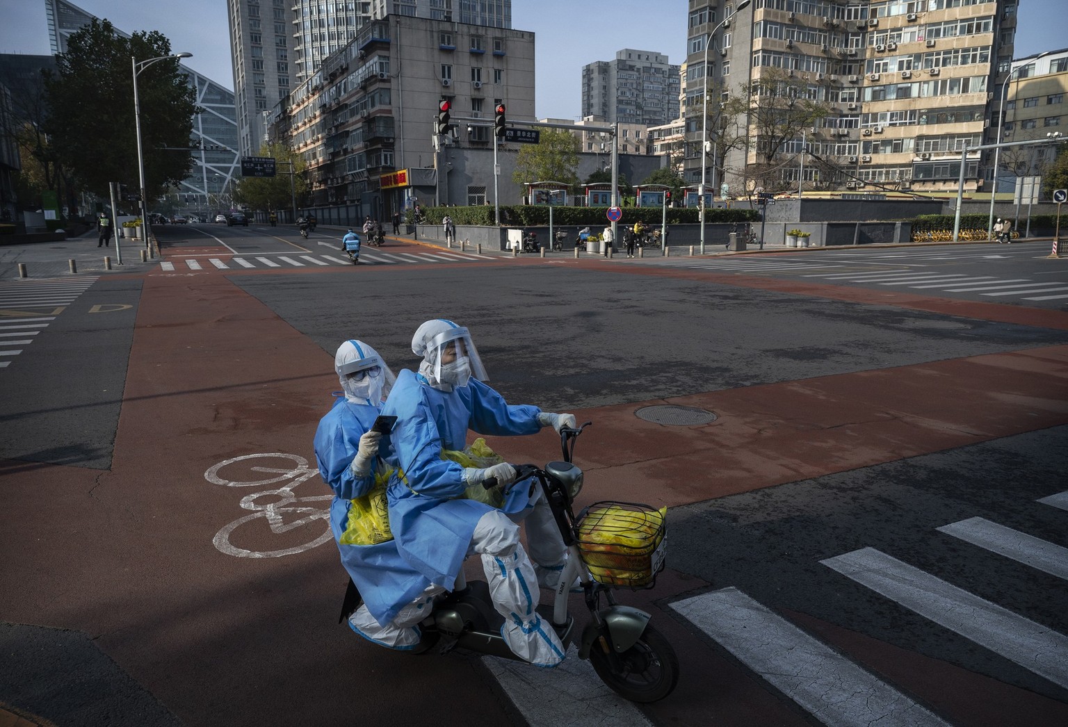 BEIJING, CHINA - NOVEMBER 23: Epidemic control workers who perform nucleic acid tests wear protective clothing to protect against the spread of COVID-19 as they ride shared bicycles in a nearly empty ...