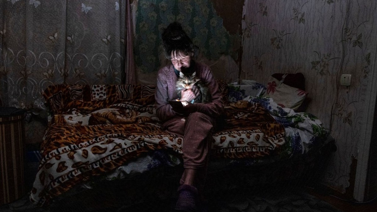 BORODYANKA, UKRAINE - OCTOBER 20: Tetyana Safonova, 61, sits with her cat Asya as she looks at her mobile phone during a power outage on October 20, 2022 in Borodyanka, Ukraine. Tetyana wasn't ab ...