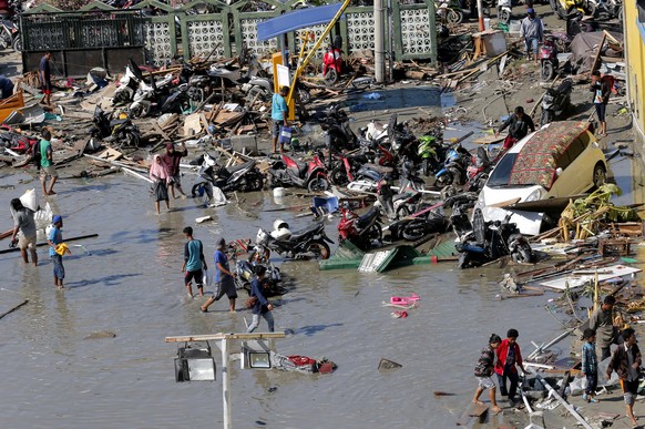 People survey outside the shopping mall which was damaged following earthquakes and a tsunami in Palu, Central Sulawesi, Indonesia, Sunday, Sept. 30, 2018. Rescuers try to reach trapped victims in col ...