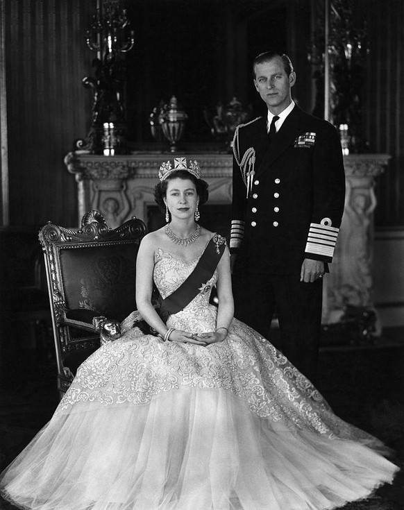 (Original Caption) Queen Elizabeth II and Prince Phillip. She is seated and wearing a crown, he is standing in uniform. Undated photograph.