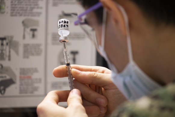 epa08887796 US Navy Corpsman Roman Silvestri holds a syringe and vial containing the Pfizer-BioNTech COVID-19 vaccine as he prepares to administer the vaccine to a healthcare worker, at Naval Medical  ...