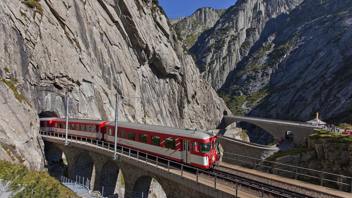 The Matterhorn Gotthardbahn, a meter-gauge railroad, driving over the so called Teufelsbruecke, "Devil's bridge", in the gorge Schoellenenschlucht and the river Reuss. canton of Uri, Sw ...