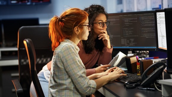 Zwei Frauen vor Computer-Bildschirmen. Symbolbild für Software-Entwicklung, IT und Cybersicherheit.