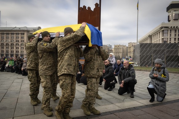 People stand kneeling as Ukrainian servicemen carry a coffin of their fellow-soldier Ruslan Ganushchak, a well-known cameraman, who was killed in the Russia-Ukraine war, during the funeral ceremony in ...