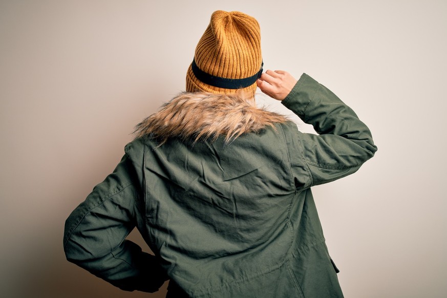 Young brunette skier woman wearing snow clothes and ski goggles over white background Backwards thinking about doubt with hand on head