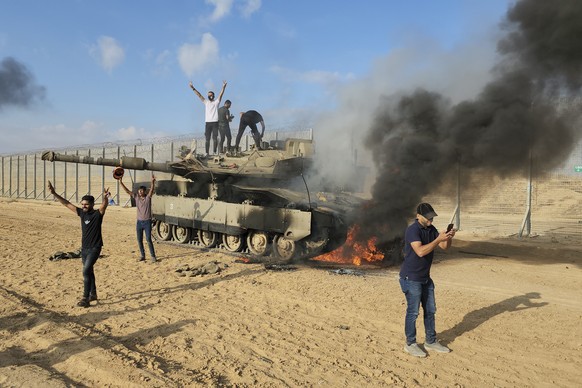 FILE - Palestinians celebrate by a destroyed Israeli tank at the Gaza Strip fence east of Khan Younis Saturday, Oct. 7, 2023. The militant Hamas rulers of the Gaza Strip carried out an unprecedented,  ...