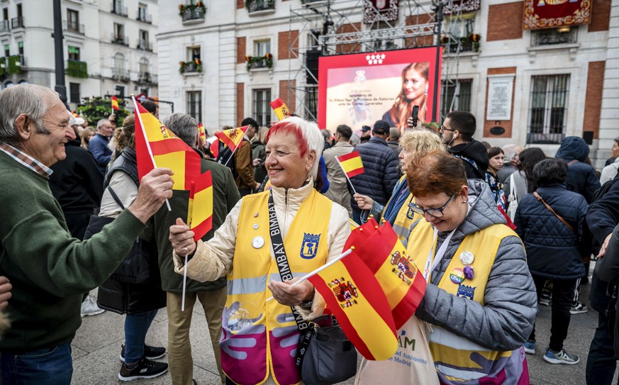 epa10950130 Women hand out Spanish flags at Puerta del Sol square as a crowd waits to see Spain&#039;s Royal Family on their way to the Lower House in Madrid, to attend the ceremony in which Spain&#03 ...