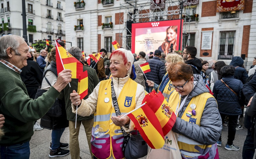 epa10950130 Women hand out Spanish flags in Puerta del Sol Square as a crowd waits for the Spanish royal family on their way to the House of Commons in Madrid, to attend the ceremony in which Spain ...