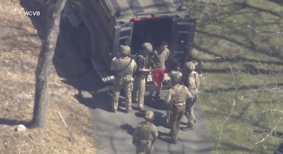 This image, taken from a WCVB-TV video, shows Jack Teixeira, in T-shirt and shorts, being taken into custody by armed tactical officers in Dighton, Massachusetts on Thursday, April 13, 2023.  (WCVB-TV v...