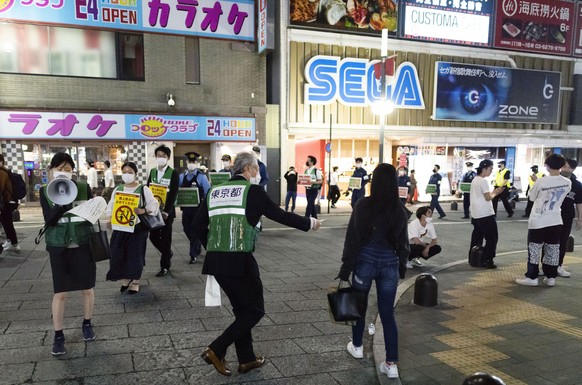 One of the Tokyo Metropolitan Government staff tries to hand out a face mask to a pedestrian as a group of government staff urges people to go home from the Kabukicho entertainment district in the Shi ...