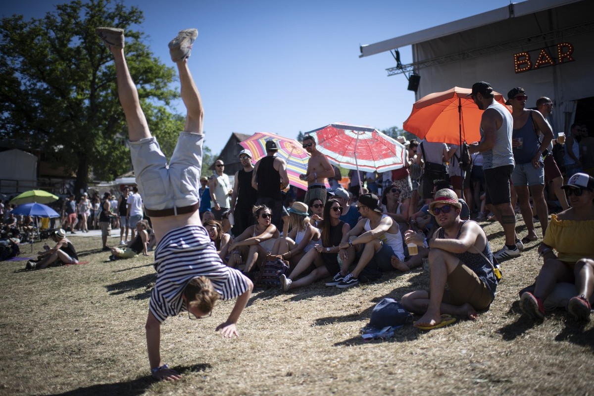 A man performs a handstand as spectators shelter from the sun on the third day of the 43. St. Gallen Openair, on Saturday, June 29, 2019, in St. Gallen, Switzerland. The music festival takes place fro ...