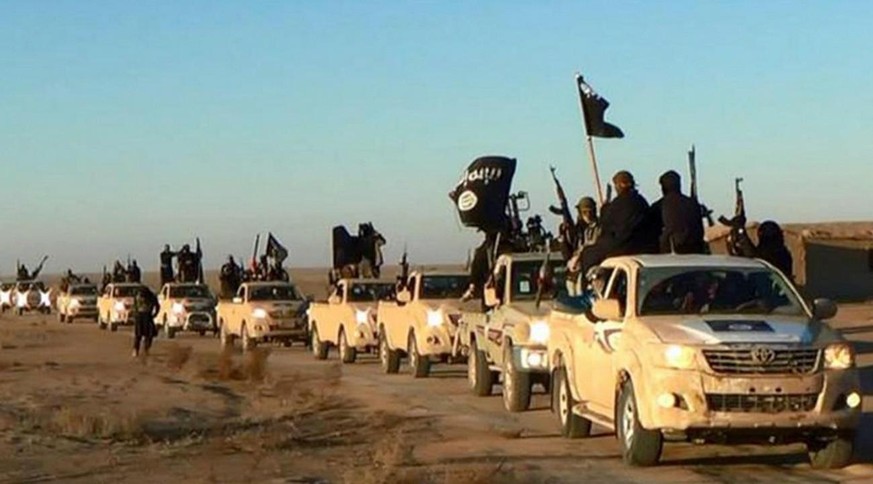 IS-Kämpfer halten ihre Waffen hoch und schwenken ihre Fahnen auf ihren Fahrzeugen in einem Konvoi auf einer Strasse, Ar-Raqqa, Syrien.