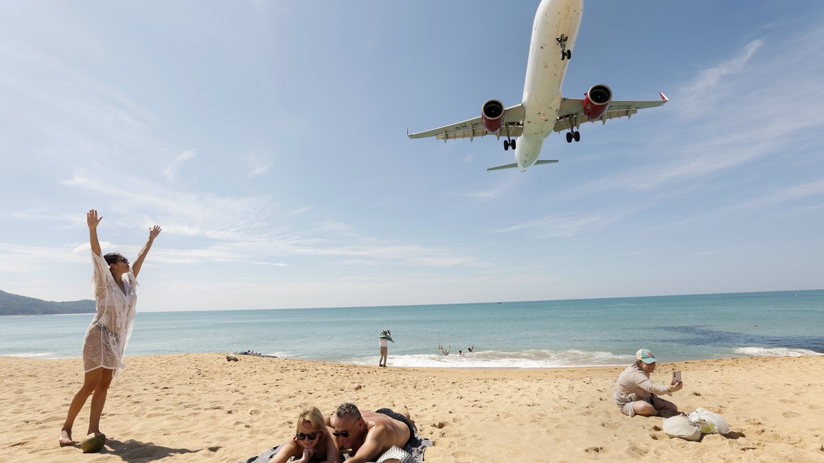 epa11792817 Tourists pose for pictures on a beach as an airplane approaches for landing at Phuket International Airport in Phuket Island, southern Thailand, 25 December 2024. This year Thailand has we ...