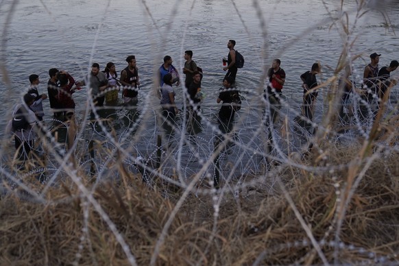 FILE - Migrants wait to climb concertina wire after crossing the Rio Grande and entering the U.S. from Mexico, Sept. 23, 2023, in Eagle Pass, Texas.  A divided Supreme Court on Tuesday, March 1…