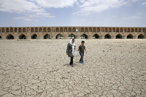 FILE - A woman and a boy walk on the dried up riverbed of the Zayandeh Roud river that no longer runs under the 400-year-old Si-o-seh Pol bridge, named for its 33 arches, in Isfahan, Iran on July 10,  ...