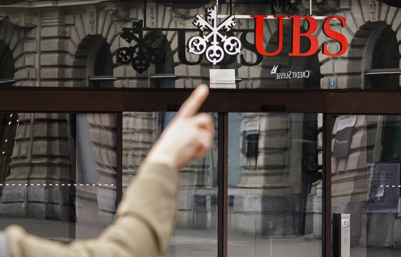 epa10532202 A man points at the logos of the Swiss banks Credit Suisse and UBS at Paradeplatz in Zurich, Switzerland, 19 March 2023. Shares of Credit Suisse lost more than one-quarter of their value o ...