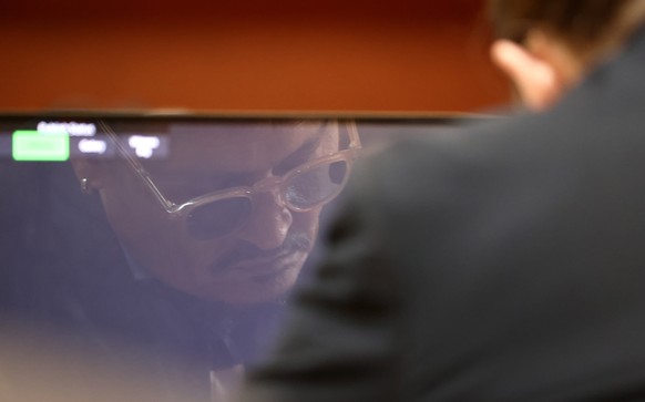epa09929093 US actor Johnny Depp is reflected in a computer screen as Amber Heard testifies on the stand during the 50 million US dollar Depp vs Heard defamation trial at the Fairfax County Circuit Co ...