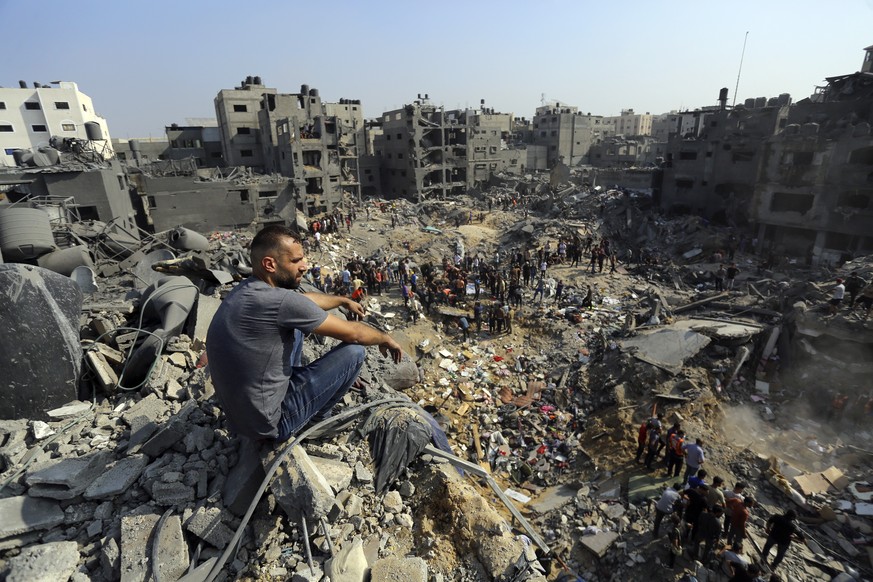 A man sits on the rubble as others wander among debris of buildings that were targeted by Israeli airstrikes in Jabaliya refugee camp, northern Gaza Strip, Wednesday, Nov. 1, 2023. (AP Photo/Abed Khal ...