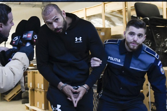 FILE - A police officer escorts Andrew Tate from the Directorate for Investigating Organized Crime and Terrorism (DIICOT) after prosecutors examined electronic equipment confiscated during the investi ...