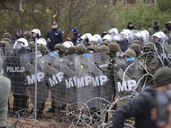 FILE - Polish police and military police stand behind the border fence as migrants from the Middle East and elsewhere gather at the Belarus-Poland border near Grodno, Belarus, Monday, Nov. 8, 2021. Th ...