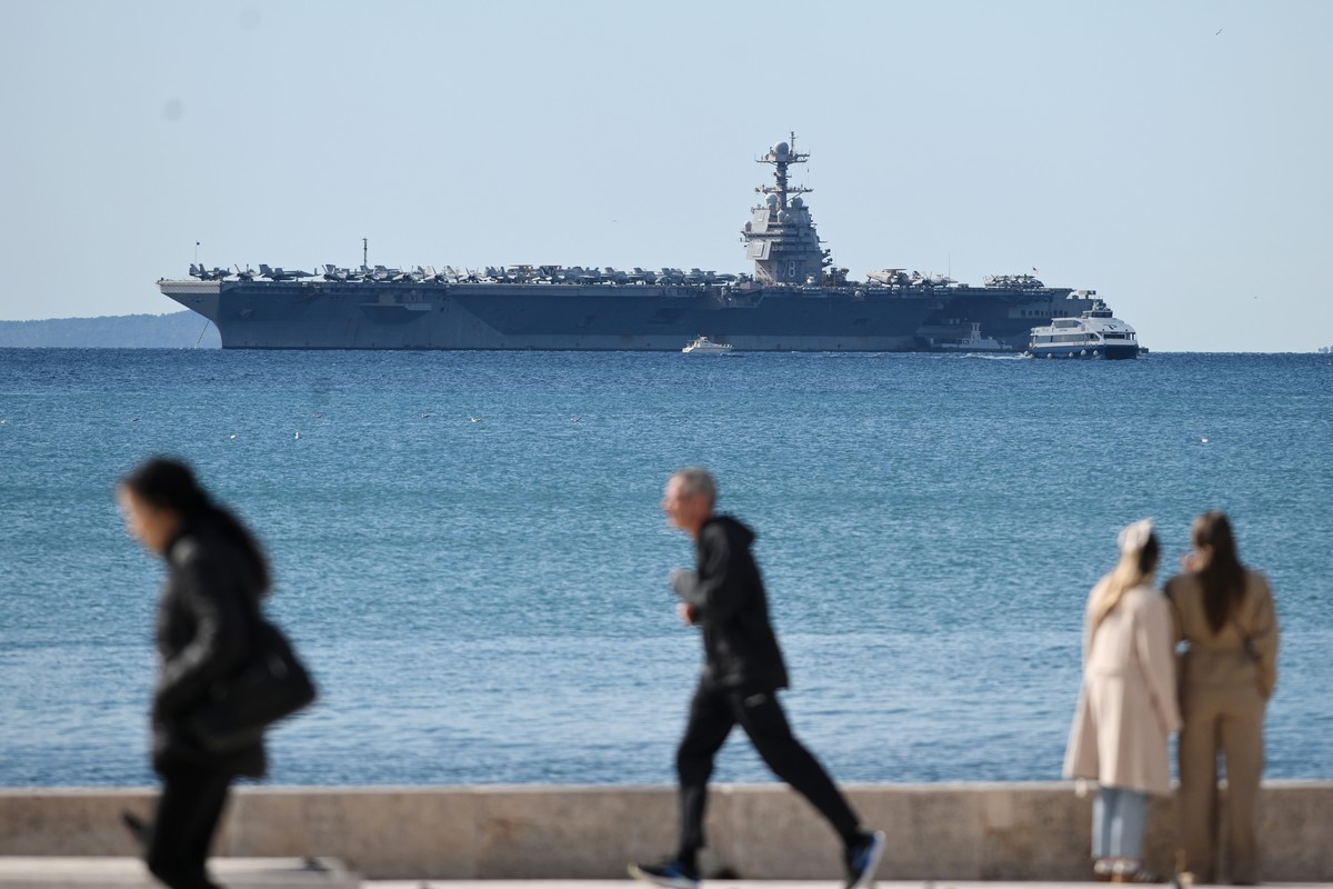 epa12858438 Pedestrians pass by as the US Navy aircraft carrier USS Gerald R. Ford (CVN-78) sits anchored in Split, Croatia, 29 March 2026. The ship arrived for repairs following a non-combat fire dur ...